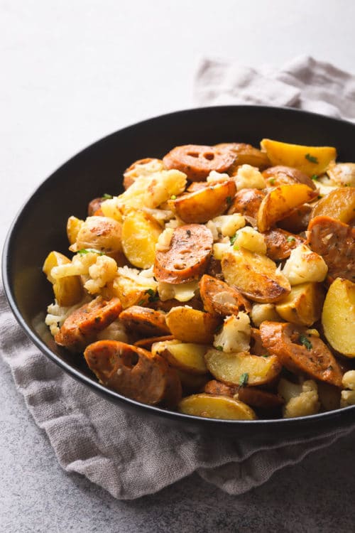 A flavorful skillet sausage and potatoes in a large black serving bowl.