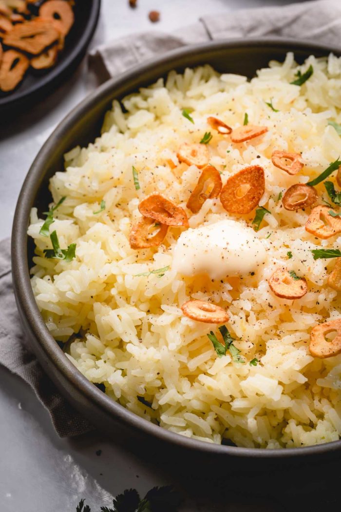 A shallow bowl of garlic butter rice topped with garlic chips, slice of butter and fresh herbs.