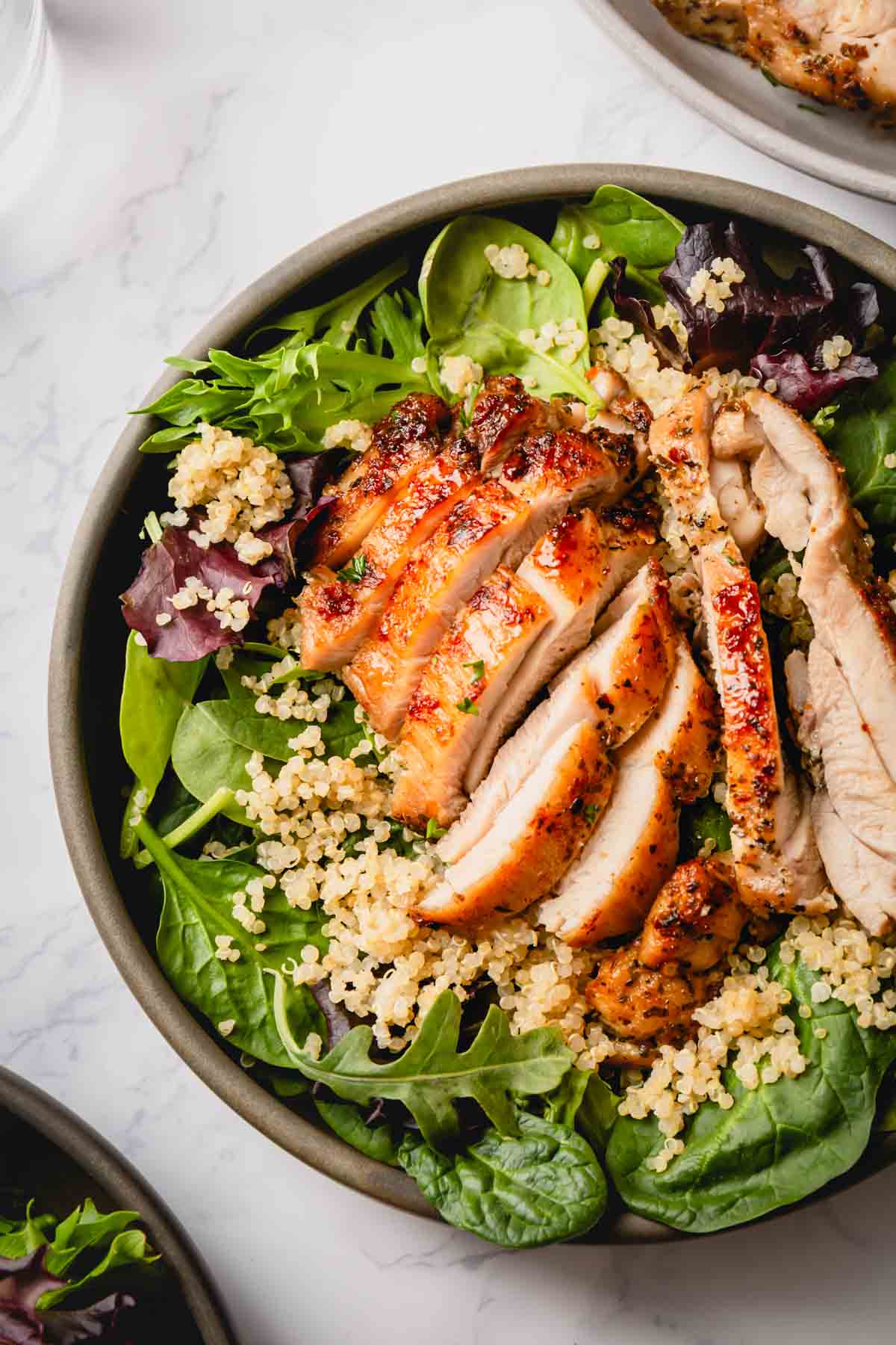 Green salad topped with quinoa and sliced chicken thighs.