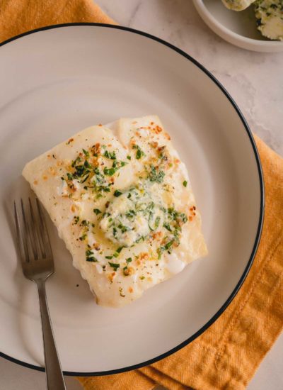 Baked cod filet with lemon pepper butter on a white plate.