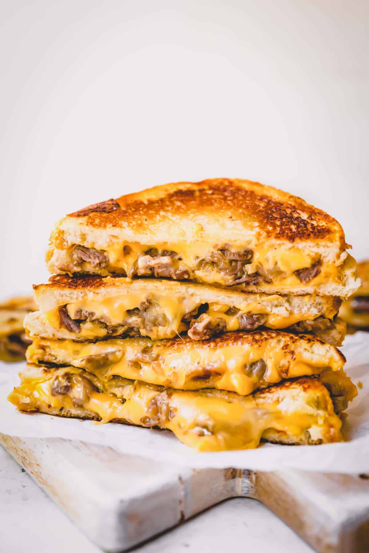 Halved Philly cheesesteak grilled cheese sandwiches staked on top of each other.