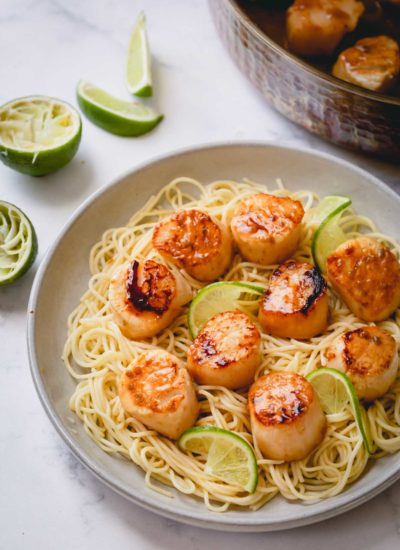 Seared scallops over a bed of angel hair pasta on a white plate.
