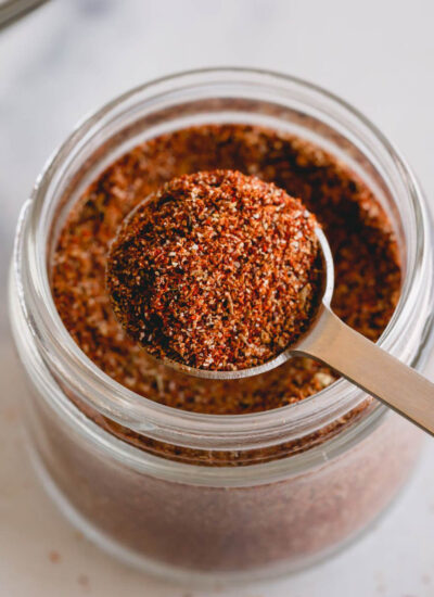 A tablespoon scooping homemade taco seasoning from a spice jar.