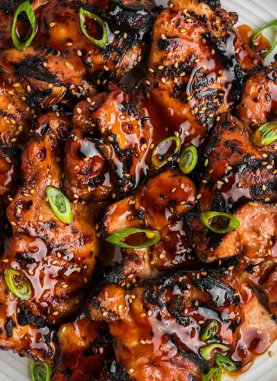 Overhead image of grilled teriyaki chicken topped with scallions and sesame seeds on a plate.